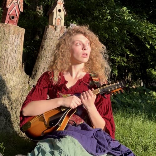 Natalie Starr Storyteller ORF A woman sitting in the woods with a mandolin